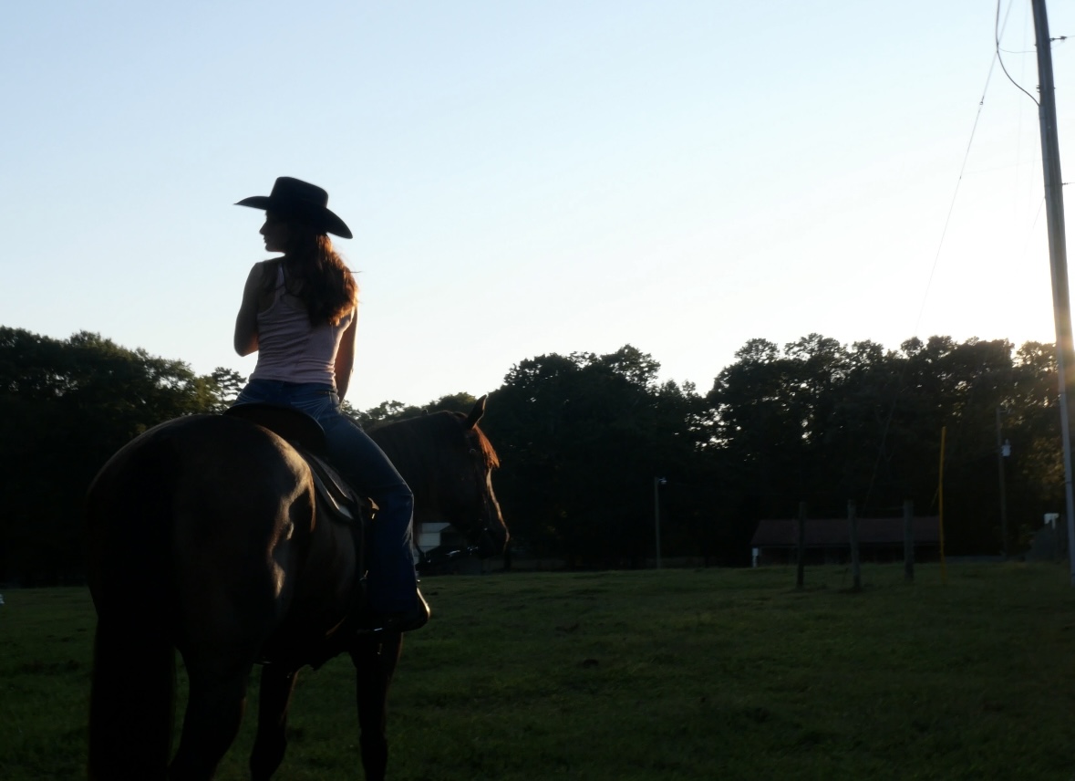 Rider on horseback at golden hour with a rustic barn in the distance